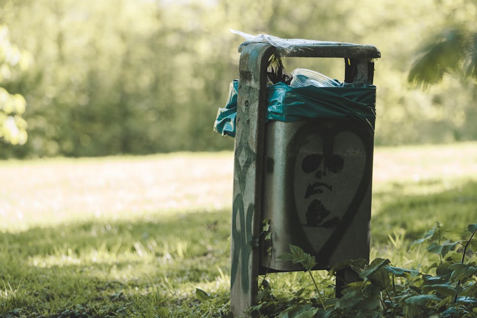 A row of purple garden waste bags made from plastic, tightly tied with pink and purple cords, are placed on a grassy lawn near a hedge. The lawn features a mixture of freshly cut, trimmed grass and pa